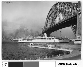 P&O liner STRATHEDEN arriving in Sydney and passing under the Sydney Harbour Bridge with a tug boat seen at the liner’s stern