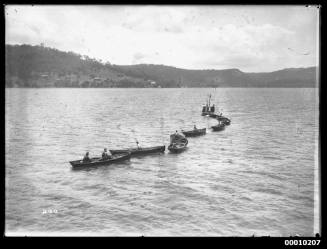 Row of nine rowing boats being towed to starting area