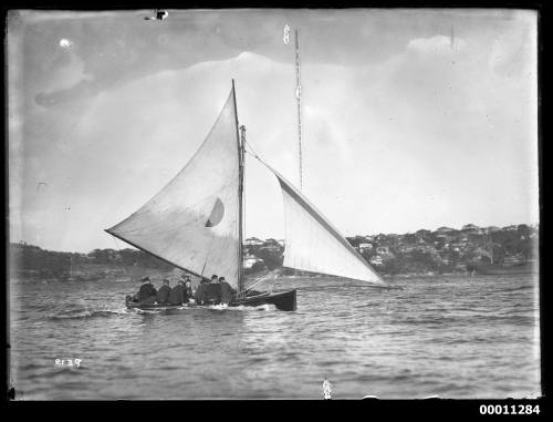 18-footer ROSETTA with at least nine crew visible, sailing on Sydney Harbour with Vaucluse shore in background