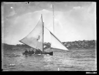 18-foot skiff with at least nine crew visible, sailing on Sydney Harbour with Vaucluse shore in background