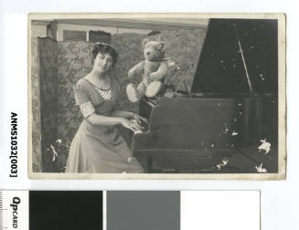 Photographic postcard of a woman, possibly actress Marjorie Neil, and toy bear at a piano