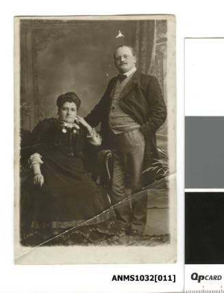 A man and a woman, with the woman sitting in a chair, and the man standing beside her