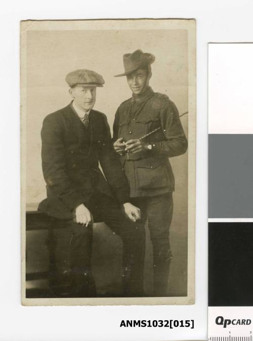 Postcard featuring a black and white photograph of two men, one is a suit and hat sitting, and the man on the right in army uniform