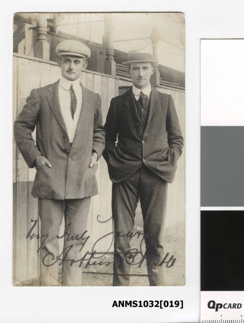 Postcard featuring a black and white photograph of two men in suits and wearing hats, with their hands in their pockets