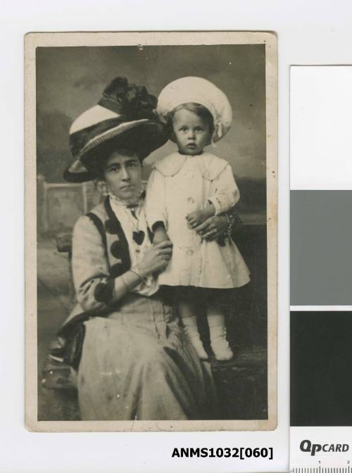 A woman, Elsie, wearing a large hat with her son standing on a chair beside her