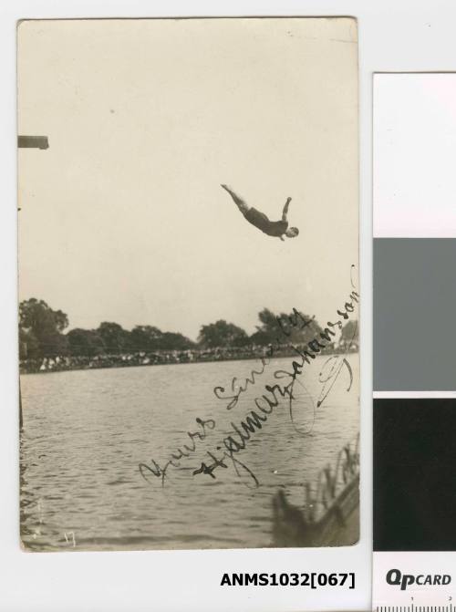 A man mid dive, in the air above the water, having dived off a diving board