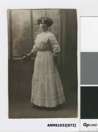 A woman standing beside a window, wearing a white dress
