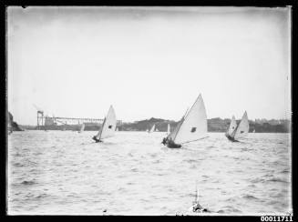Skiffs racing with construction on the Sydney Harbour Bridge visible in the background