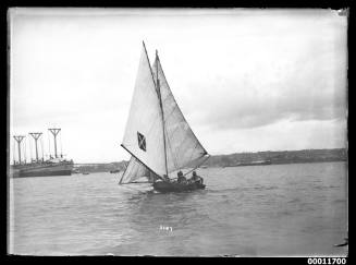 18-foot skiff MASCOTTE on Sydney Harbour, HMAS  MOMBAH at left