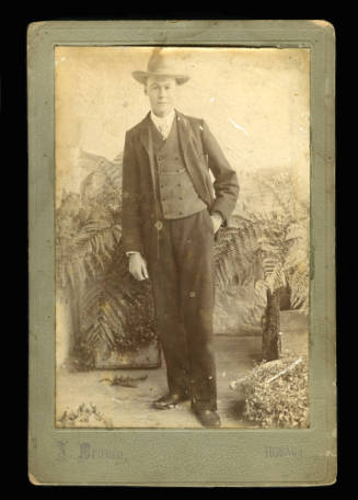 Man standing, wearing a suit and hat, with one hand in his pocket