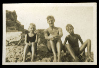 Man and two young boys sitting on a rocky section of beach in their swim suits