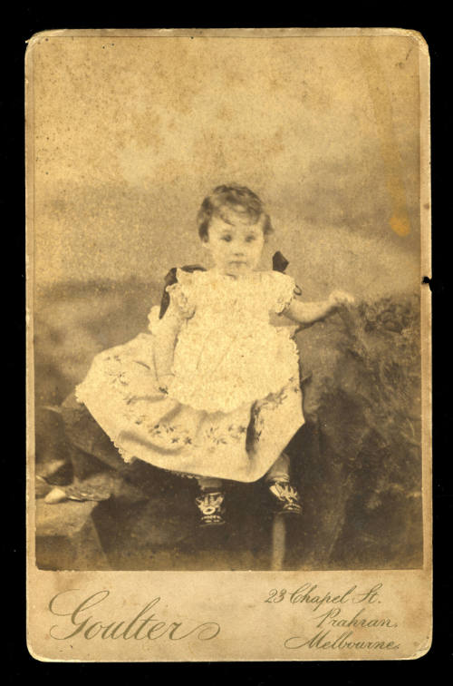 Young girl sitting on a rock, wearing a white dress and black and white shoes