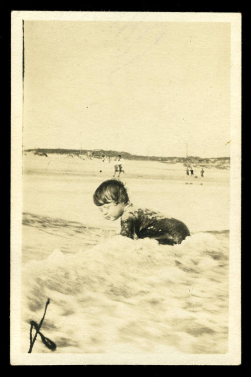 Small boy at the beach, crawling on the sand with a wave crashing on his back