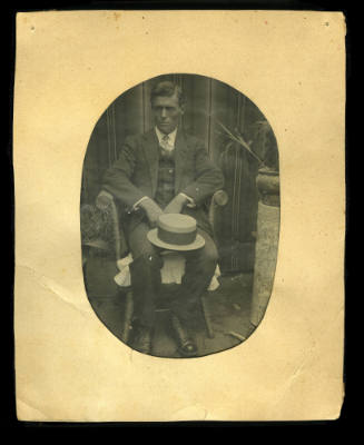 Man sitting in a chair with his hat resting on his knees, and his hands together in his lap