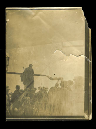 A group of people standing, with one man higher in the air, perhaps standing on a platform