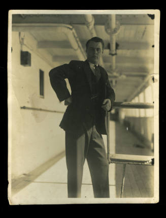 Man in a dark coloured suit leaning on a metal railing, with pipes running along the ceiling above him