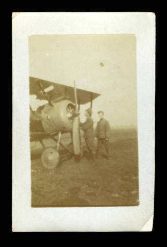 Black and white photograph of two men in uniform standing in front of a plane on a field