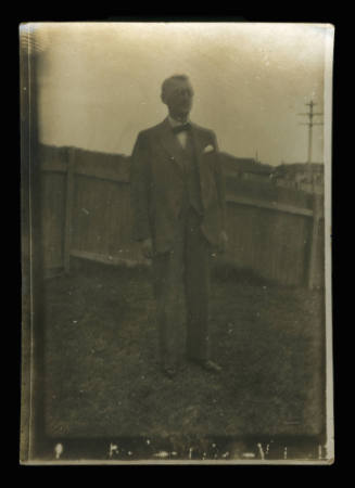 An elderly man standing in a backyard in front of a wooden fence