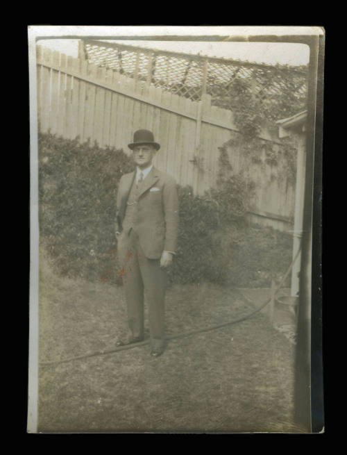 Man standing on a grassed area in a backyard, with a wooden fence in the background