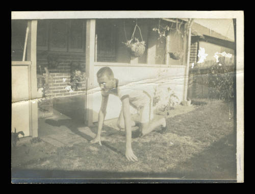 Man on his hands and knees on the grass next to a house, about to run