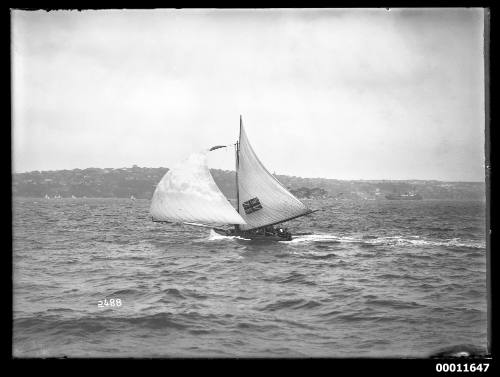 18-foot skiff AUSTRALIA sails with main and ballooning headsail on rough Sydney Harbour, note length of bowsprit, stowed in sections