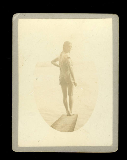 Photograph of a woman in a swimsuit, presumably Beatrice Kerr, with her right hand on her hip, standing on a diving board, facing over her shoulder to the camera