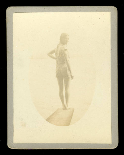 Photograph of a woman in a swimsuit, presumably Beatrice Kerr, with her right hand on her hip, standing on a diving board, facing over her shoulder to the camera