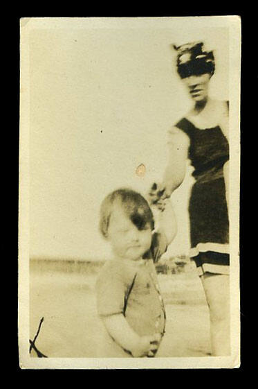 Woman, Beatrice Kerr's sister, holding the hand of a small child, on a beach