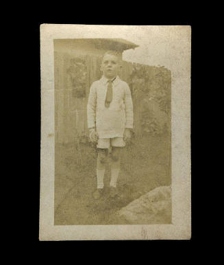 Young boy standing in front of a wooden fence, probably the son of Beatrice Kerr