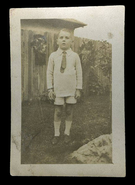 Young boy standing in front of a wooden fence probably the son of