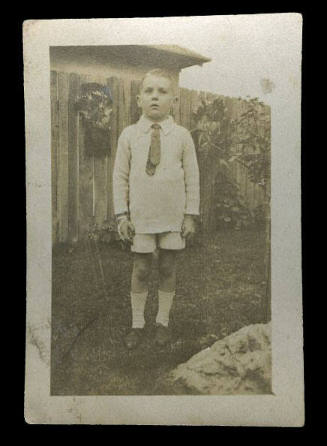 Young boy standing in front of a wooden fence, probably the son of Beatrice Kerr