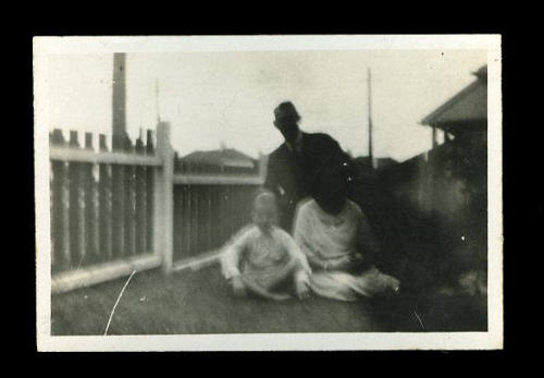 Man, woman and child sitting or kneeling in a group on the lawn next to a picket fence