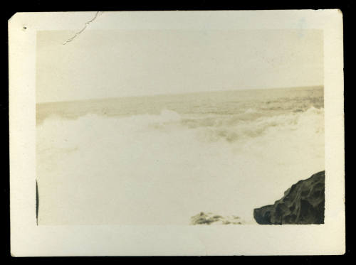 Black and white photograph of waves in the ocean, with a rock visible on the bottom right hand corner of the photo