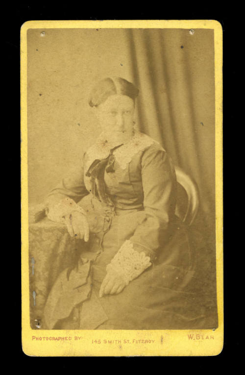 Woman in a sitting pose, wearing a long dress with lace cuffs and collar