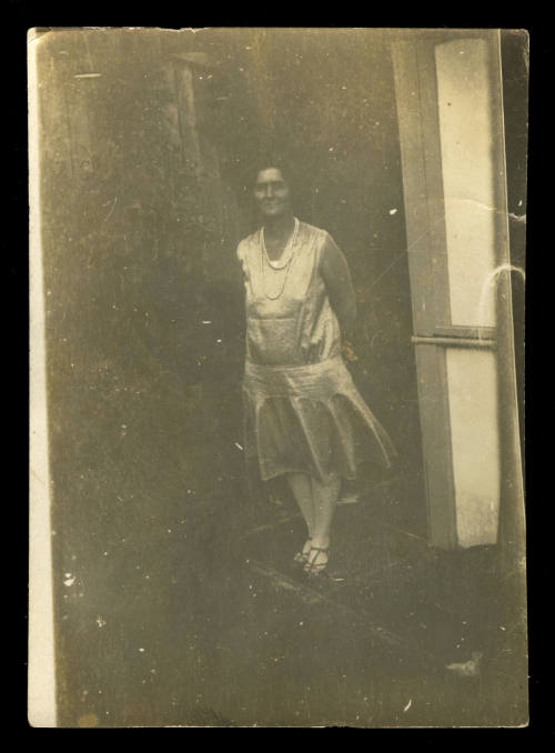 Woman standing with her arms behind her back, wearing a sleeveless dress and sandals