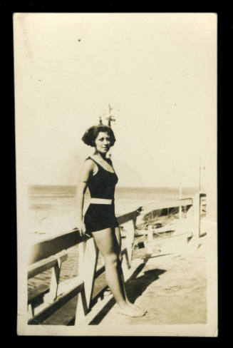 Woman wearing a black swimsuit resting on a wooden fence beside the water