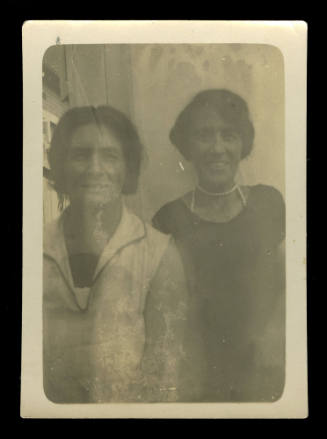Black and white photograph of two women, the one on the left wearing a white shirt, and the lady on the right wearing a black shirt with a pearl necklace