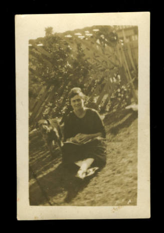 Woman, probably Beatrice Kerr, sitting on the grass wearing a black dress, with a dog beside her