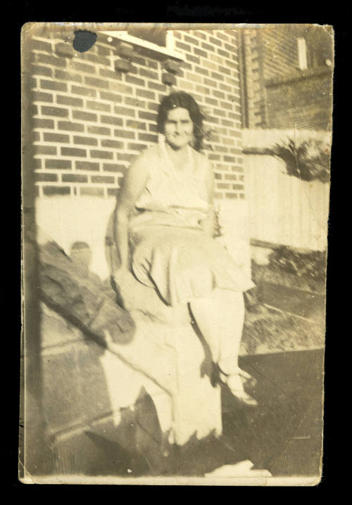 Woman sitting on the edge of a wall, wearing a pale coloured sleeveless dress, probably Beatrice Kerr