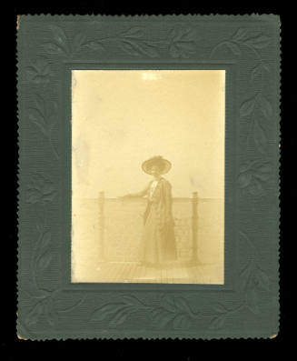 Woman, probably Beatrice Kerr, standing with her arm on the fence of a pier