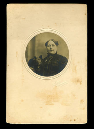 Middle aged woman in black clothing, holding a dog beside her
