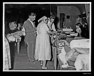 Two men and a woman examine clothing on table