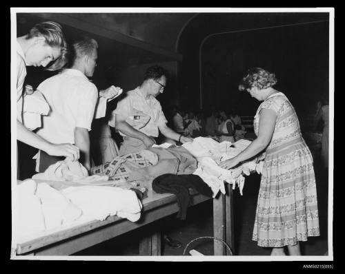 Group of men examine clothes on table while a woman watches