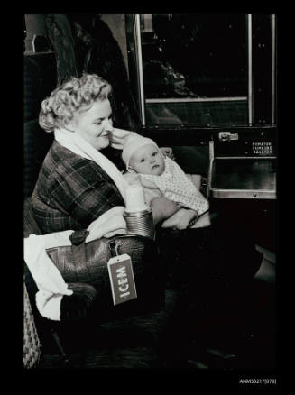 Young woman seated in railway carriage with baby in arms