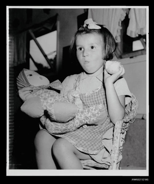 Young girl holding rag doll eating fruit, European displaced persons camp