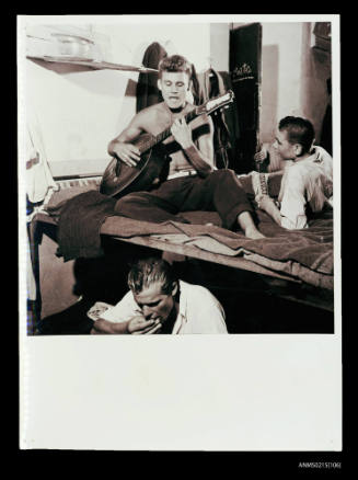 Three young men in dormitory, one playing guitar, displaced persons camp Europe