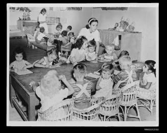 Young children seated at two tables playing with pencils and papaer, displaced persons camp Europe