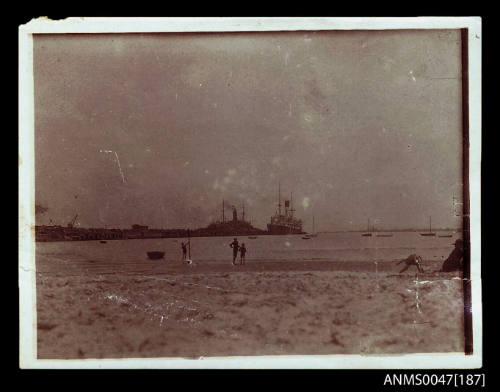 Harbour beach, two large steamships docked at a wharf jetty in distance