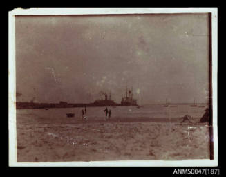 Harbour beach, two large steamships docked at a wharf jetty in distance