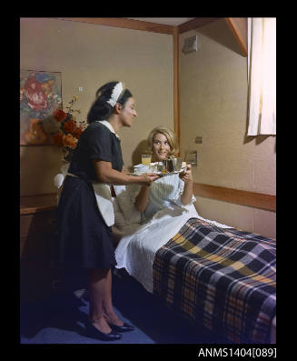 Photographic transparency showing a passenger aboard the ship FLAVIA being served breakfast in bed by a stewardess